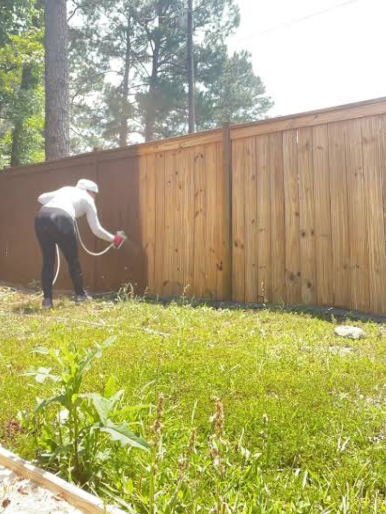 Creativo Painting crew member spray-staining a wood privacy fence in a backyard