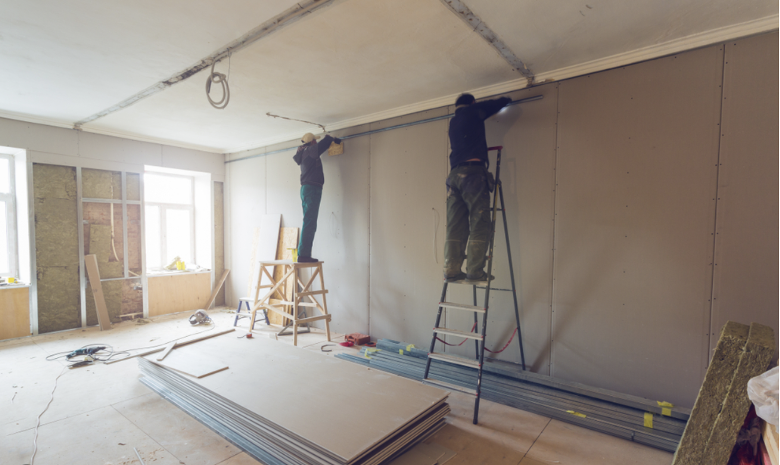 Crew hanging new sheetrock panels on walls and ceiling of a room addition